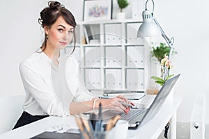 Young businesswoman sitting at her workplace, working out new business ideas, wearing formal suit and glasses, looking