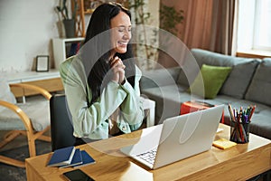 Young businesswoman sitting at home with laptop with happy and excited face, booking trip online via travel services