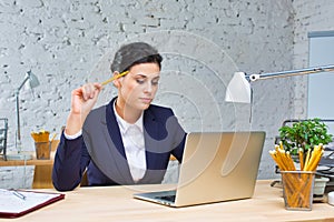 Young businesswoman sitting with laptop at desk against brick wall in office