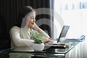 Young businesswoman sitting in modern living room and working with laptop. Remote work concept