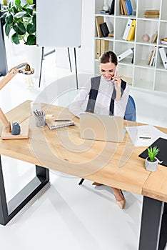 Young businesswoman sitting in office at her desk, talking on smartphone