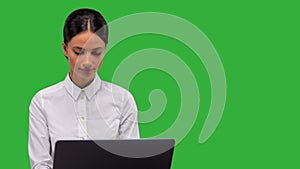 Young businesswoman sitting, typing on her laptop , isolated on green background