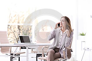 Young businesswoman with smart phone sitting in office chair at workplace