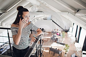 Young businesswoman is standing in cafe and talking on cell phone. Girl is waiting for friends, colleagues in restaurant