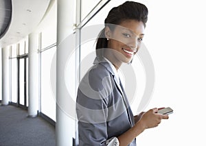 Young Businesswoman Standing In Corridor Of Modern Office Building Using Mobile Phone