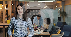 Young businesswoman standing in the modern office, smiling and looking into the camera. Working people on the blurred