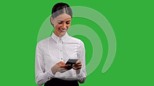 Young businesswoman standing, smiling and typing on her phone, isolated on green background