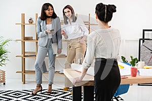 Young businesswoman standing at table and smiling colleagues talking behind