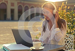 Young businesswoman or student holding headset and looking to her laptop at cafe