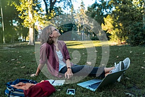 Young businesswoman student working on her notebook in park. Freelancer female sitting on grassy lawn using laptop computer with