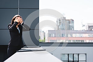 young businesswoman, suffering from fear of heights, standing on rooftop and covering face with hands.