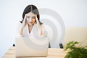 Young businesswoman suffering from headache in front of laptop at office