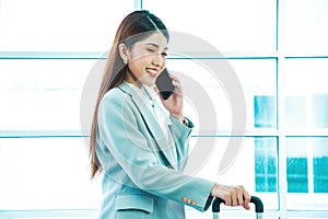 Young businesswoman in a suit pulling a suitcase and talking on the cell phone.