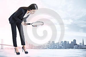 Young businesswoman in suit using magnifier