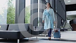 Young businesswoman with suitcase in hand smiling and walking in airport interior spbi.