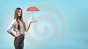 A young businesswoman supports a small open red umbrella on his open palm.