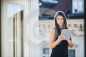 Young businesswoman with tablet standing on a terrace outside an office in city.