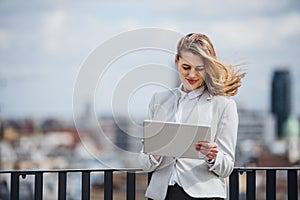 A young businesswoman with tablet standing on a terrace, working.