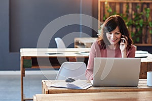 Young businesswoman talking on her cellphone and using a laptop