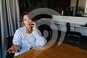 Young businesswoman talking on mobile phone while sitting at table in office