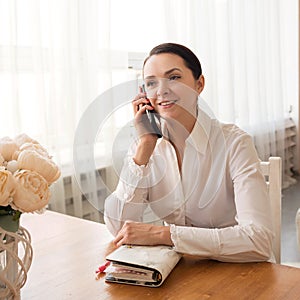 Young businesswoman talking on the phone and holding a notebook at home