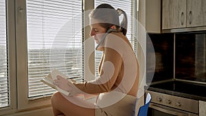 Young businesswoman talking by phone in kitchen and taking notes in notebook. Concept of education, female working in office,