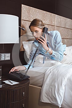 young businesswoman talking by phone while lying on bed in hotel