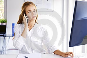 Young businesswoman talking with somebody on her mobile phone while sitting at office desk