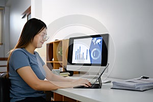 Young businesswoman using digital tablet and working with financial graph on computer monitor at home