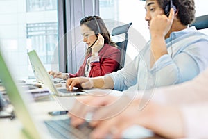 Young businesswoman using headset and laptop with colleagues in foreground at office