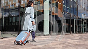 Young businesswoman walking along city street and holding suitcase in hand on autumn day spbi.