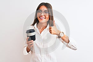 Young businesswoman wearing glasses drinking coffee over isolated white background happy with big smile doing ok sign, thumb up