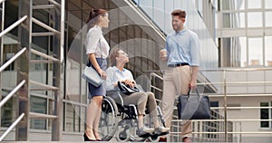 Young businesswoman in wheelchair talking with colleagues outside business center