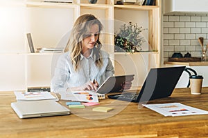 Young businesswoman woman is sitting at kitchen table and uses tablet computer, working, studying.