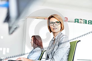 Young businesswoman working on computer with colleague in background at office