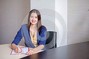 Young businesswoman working at desk in office, taking notes into personal calendar, smiling.