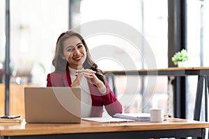 Young businesswoman working at her laptop and going over paperwork while sitting at a desk in an office