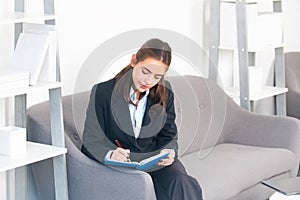 Young businesswoman working on laptop with too much work in office. Secretary girl making notes in note book.