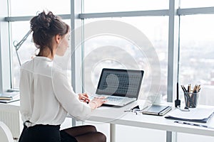 Young businesswoman working in office, typing, using computer. Concentrated woman searching information online, rear