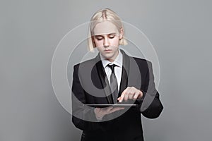 Young businesswoman working online with a digital tablet while standing against grey studio wall banner background