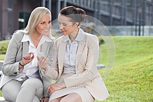 Young businesswomen with mobile phone sitting against office building