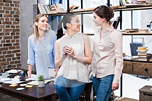 Young businesswomen talking at workplace while having coffee break