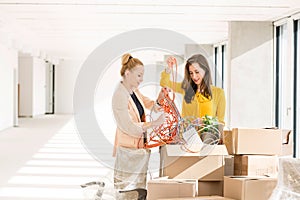 Young businesswomen untangling cords while standing by cardboard boxes in new office