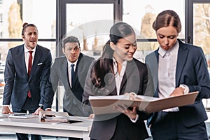 Young businesswomen working together while businessmen grimacing behind