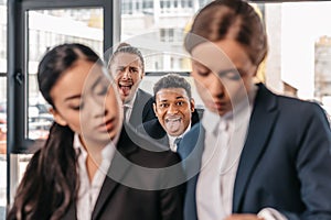 Young businesswomen working together while businessmen grimacing behind