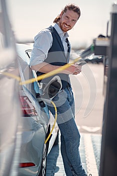 Young busnessman waiting for his electric car to charge