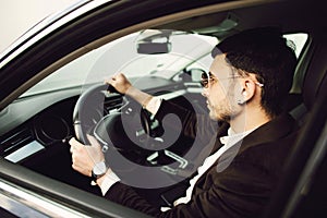 Young bussinesman in suit and black glasses driving his car. Bussines look. Test drive of the new car