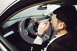 Young bussinesman in suit and black glasses driving his car. Bussines look. Test drive of the new car