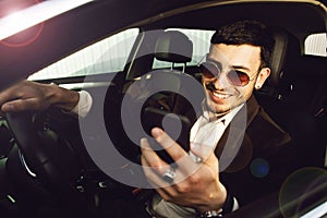 Young bussinesman in suit and black glasses speaks by phone in his car. Bussines look. Test drive of the new car