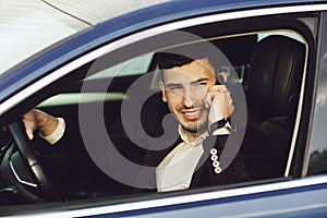 Young bussinesman in suit speaks by phone in his car. Bussines look. Test drive of the new car